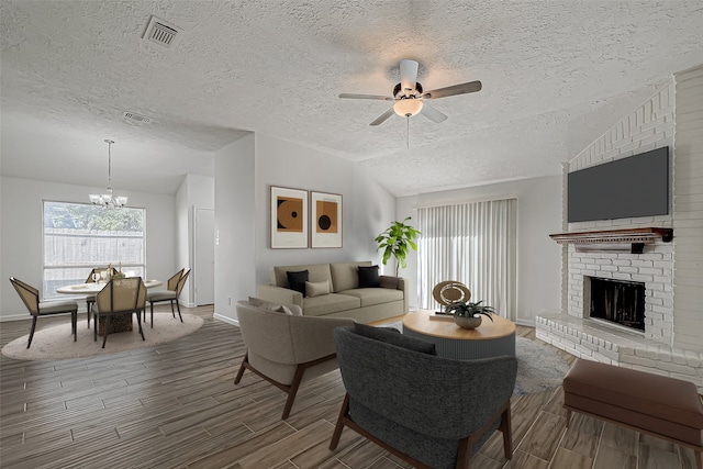 living room featuring hardwood / wood-style floors, lofted ceiling, a textured ceiling, a fireplace, and ceiling fan with notable chandelier