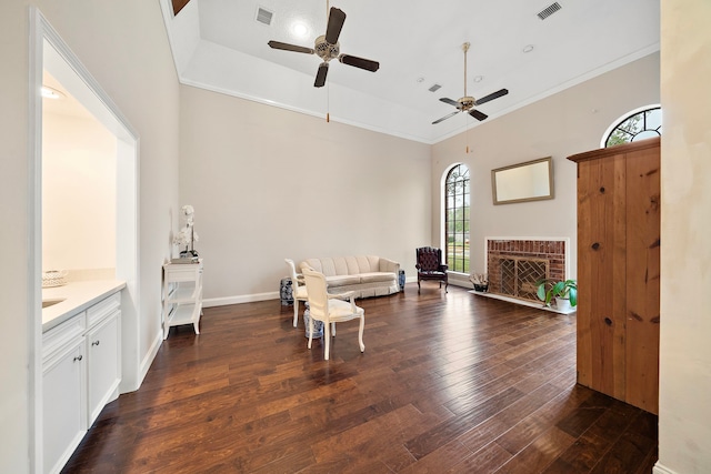 living area featuring a towering ceiling, dark hardwood / wood-style flooring, ceiling fan, crown molding, and a fireplace