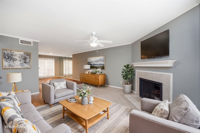 living room with a tile fireplace, crown molding, ceiling fan, and light carpet