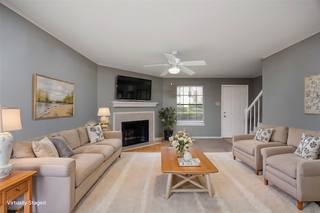 living room featuring a tile fireplace, ceiling fan, ornamental molding, and light wood-type flooring