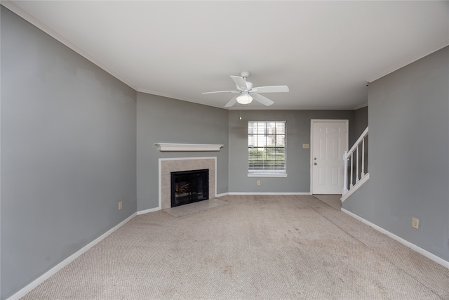 unfurnished living room with ceiling fan, crown molding, light carpet, and a tiled fireplace