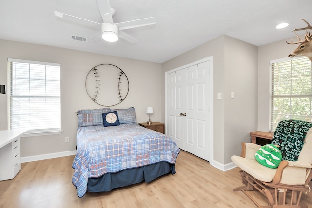 bedroom featuring a closet, light hardwood / wood-style flooring, multiple windows, and ceiling fan