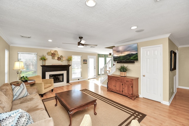 living room with a textured ceiling, ceiling fan, crown molding, and light hardwood / wood-style flooring