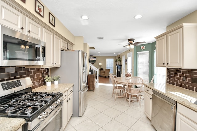 kitchen featuring cream cabinetry, light stone counters, light tile patterned floors, and stainless steel appliances