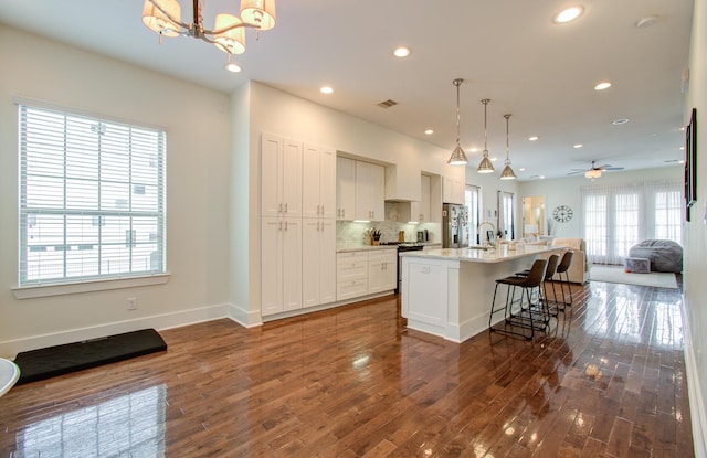 kitchen featuring appliances with stainless steel finishes, decorative light fixtures, a center island with sink, dark hardwood / wood-style floors, and a breakfast bar area