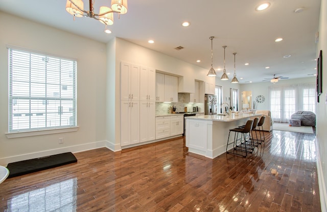 kitchen with a kitchen bar, hanging light fixtures, dark hardwood / wood-style floors, an island with sink, and white cabinets