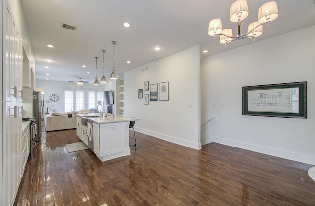 kitchen featuring dark hardwood / wood-style floors, an island with sink, decorative light fixtures, white cabinetry, and a breakfast bar area