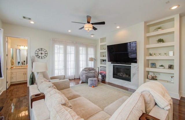 living room featuring a premium fireplace, built in features, ceiling fan, and dark wood-type flooring