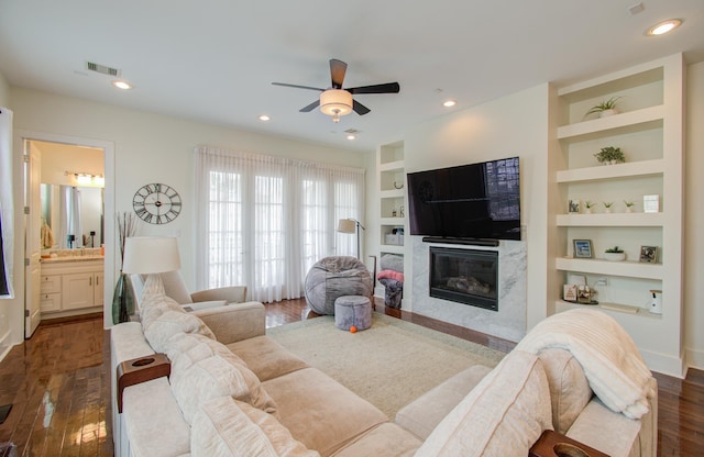 living room featuring built in shelves, ceiling fan, a premium fireplace, and dark wood-type flooring