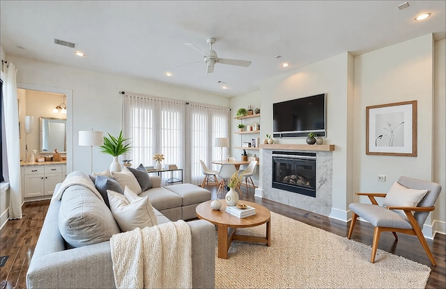 living room with dark hardwood / wood-style flooring, a premium fireplace, and ceiling fan