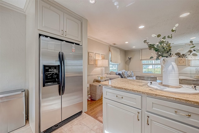 kitchen featuring stainless steel refrigerator with ice dispenser, light tile patterned flooring, white cabinetry, crown molding, and light stone counters