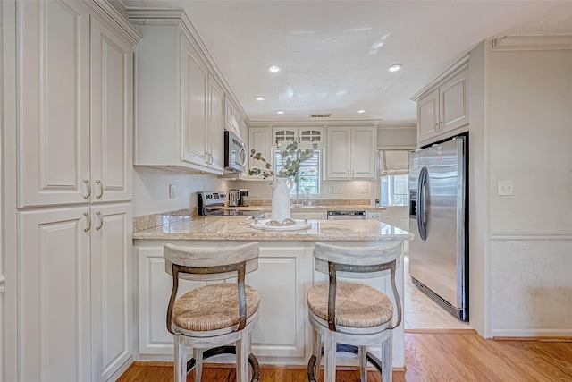 kitchen featuring sink, a kitchen breakfast bar, kitchen peninsula, stainless steel appliances, and light stone countertops