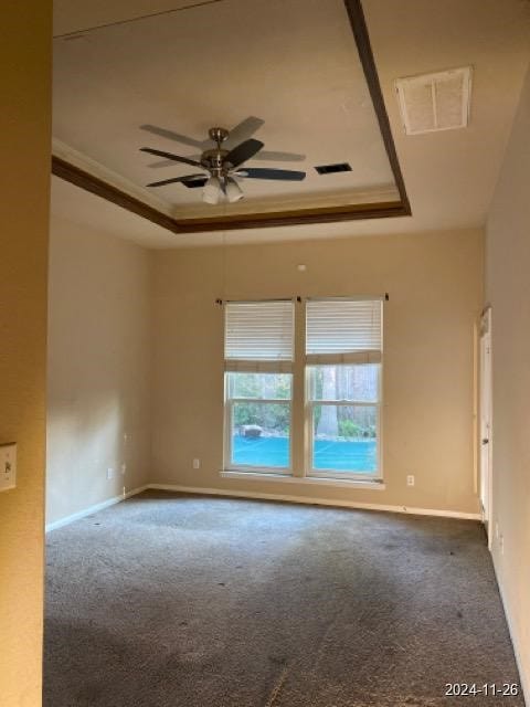 empty room featuring carpet flooring, a raised ceiling, ceiling fan, and crown molding