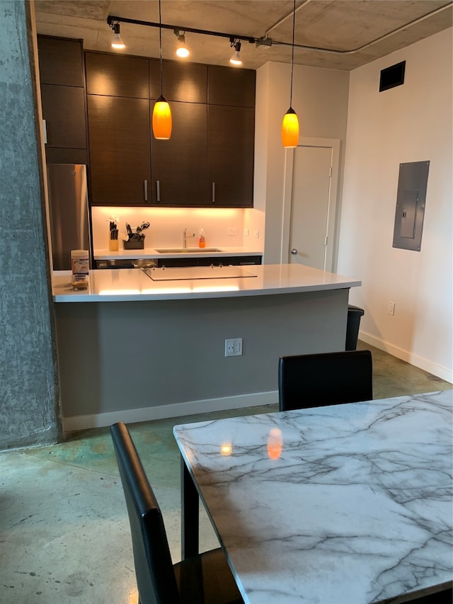 kitchen featuring stainless steel refrigerator, electric panel, concrete flooring, and decorative light fixtures