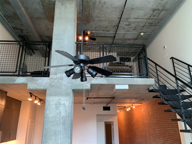 interior space with a high ceiling, rail lighting, ceiling fan, and brick wall