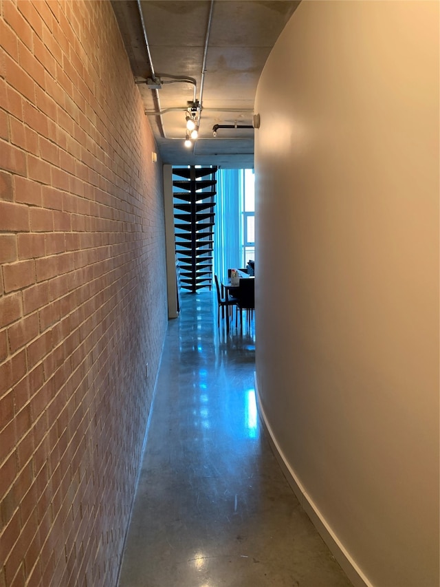 hallway featuring concrete floors and brick wall