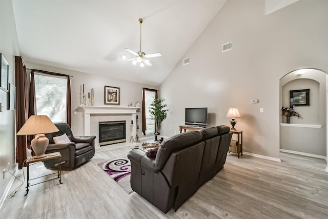 living room featuring a fireplace, light hardwood / wood-style flooring, high vaulted ceiling, and ceiling fan