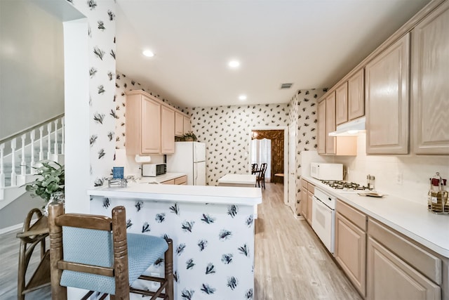 kitchen featuring white appliances, light wood-type flooring, light brown cabinetry, a kitchen bar, and kitchen peninsula