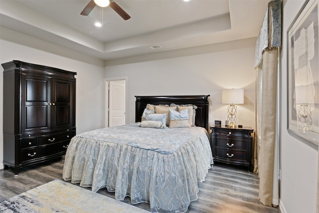 bedroom with hardwood / wood-style flooring, ceiling fan, and a raised ceiling