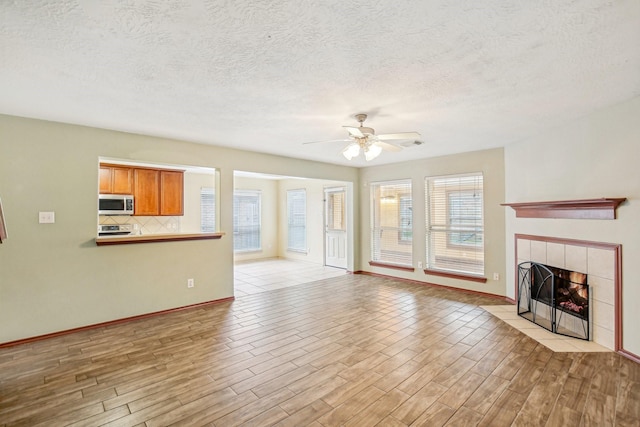 unfurnished living room with ceiling fan, a textured ceiling, and a tile fireplace