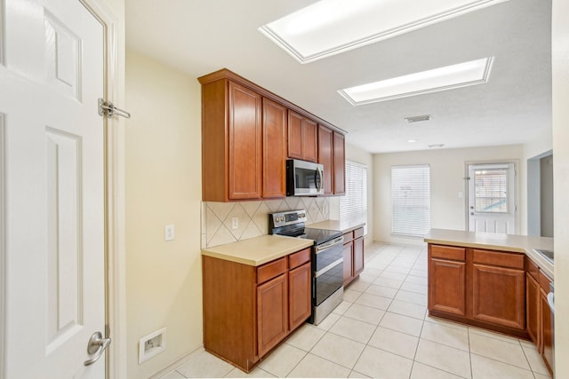 kitchen with tasteful backsplash, kitchen peninsula, light tile patterned floors, and appliances with stainless steel finishes