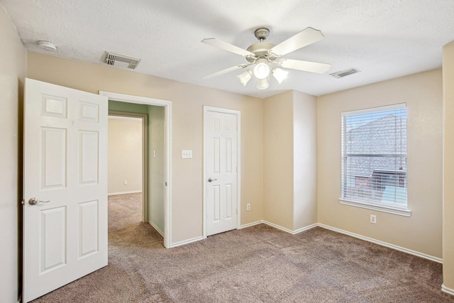 unfurnished bedroom with ceiling fan, light carpet, and a textured ceiling