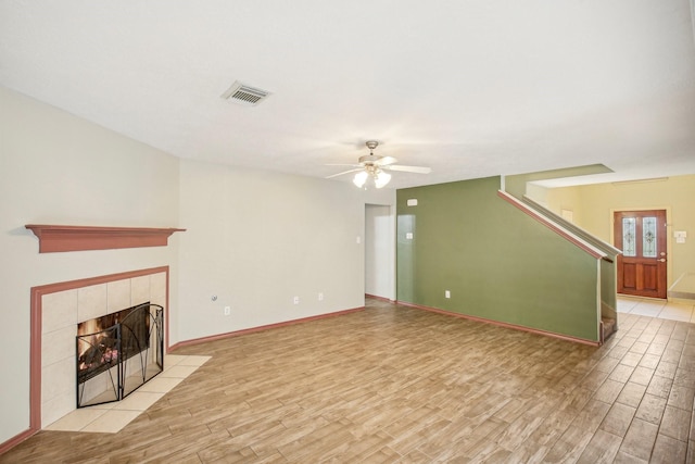 unfurnished living room featuring ceiling fan, a tiled fireplace, and light hardwood / wood-style flooring