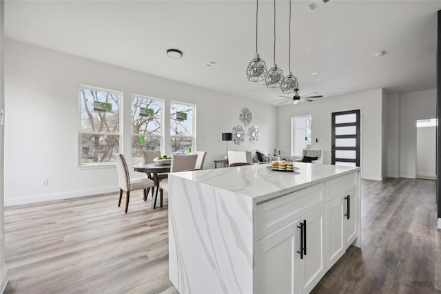 kitchen featuring light stone countertops, a center island, light hardwood / wood-style floors, white cabinetry, and hanging light fixtures