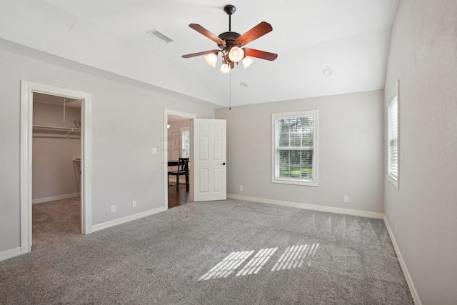 unfurnished bedroom with carpet, a walk in closet, ceiling fan, a closet, and lofted ceiling