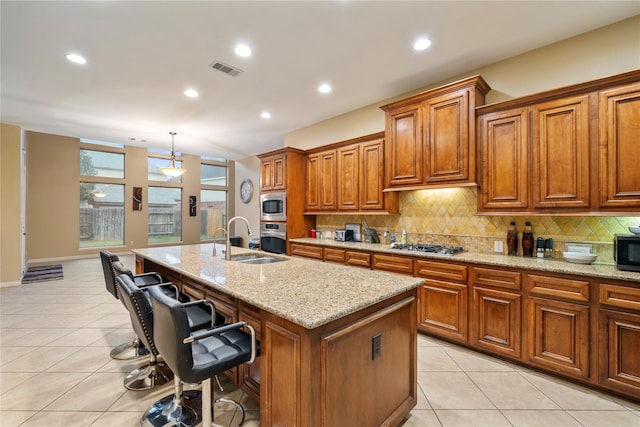 kitchen with a center island with sink, a kitchen breakfast bar, sink, appliances with stainless steel finishes, and decorative light fixtures