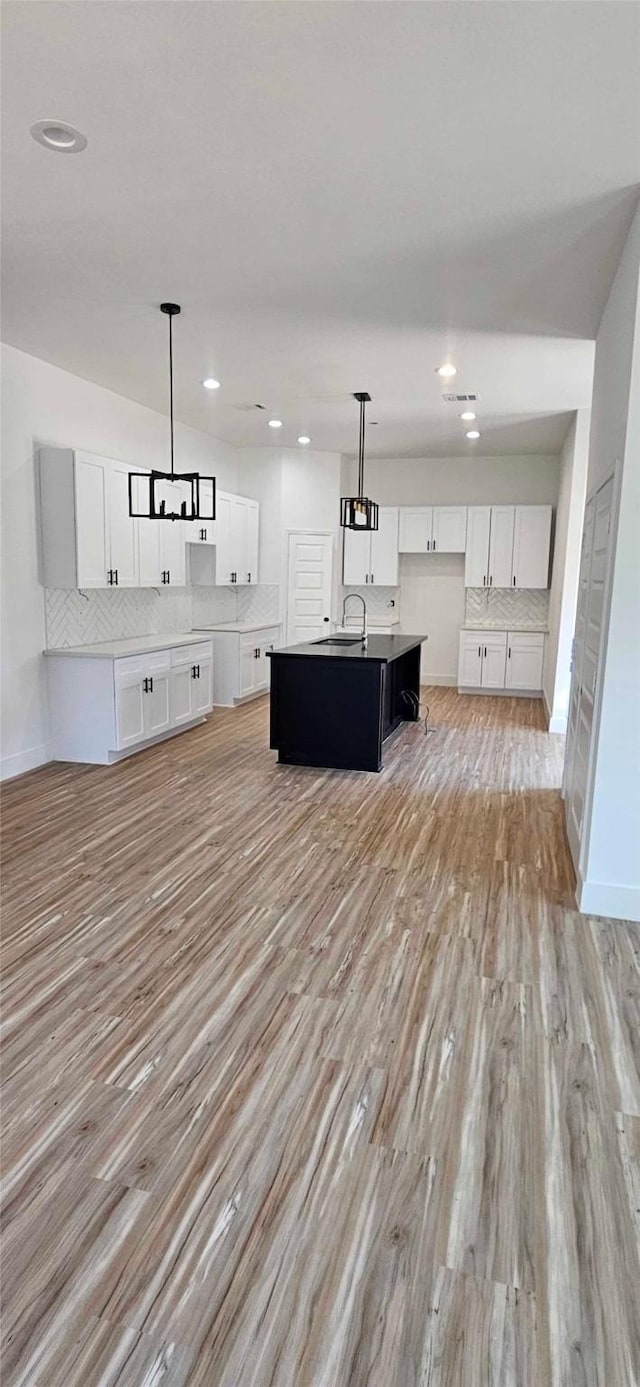 kitchen with tasteful backsplash, white cabinetry, a center island with sink, and light wood finished floors