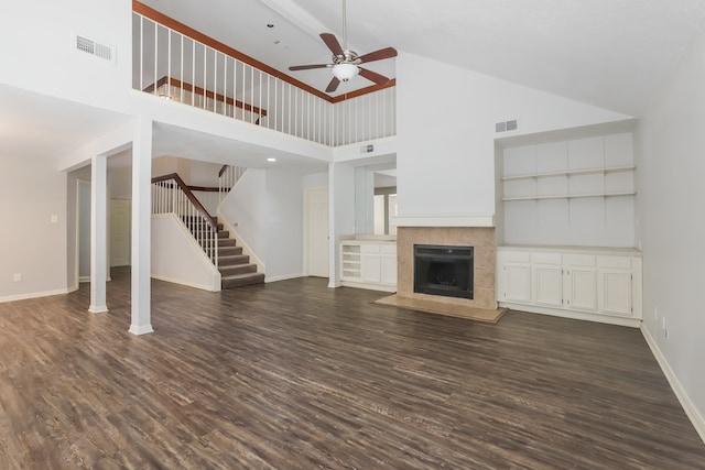 unfurnished living room with a tile fireplace, ceiling fan, built in shelves, dark hardwood / wood-style flooring, and high vaulted ceiling