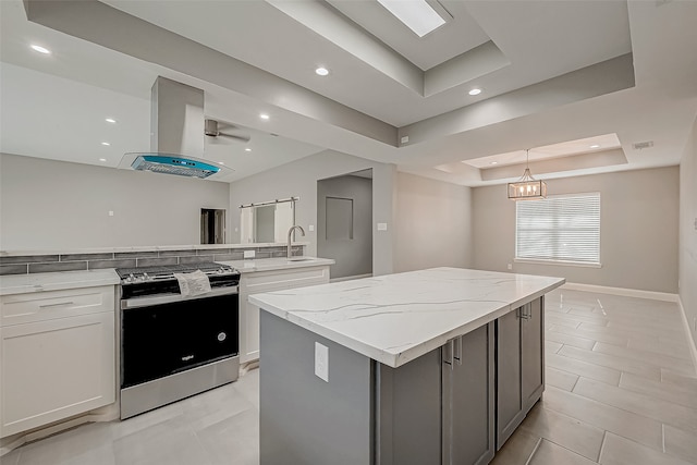 kitchen featuring ventilation hood, stainless steel stove, a tray ceiling, a kitchen island, and white cabinetry