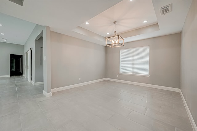 spare room with a tray ceiling, a barn door, and a notable chandelier