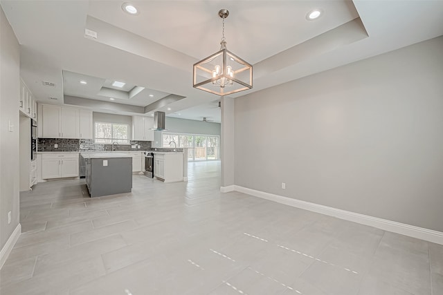 kitchen with wall chimney exhaust hood, a tray ceiling, pendant lighting, white cabinets, and a center island