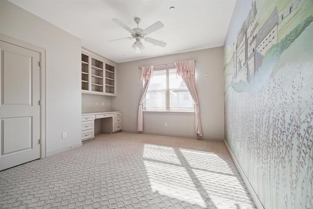 unfurnished office with ceiling fan, built in desk, and light colored carpet