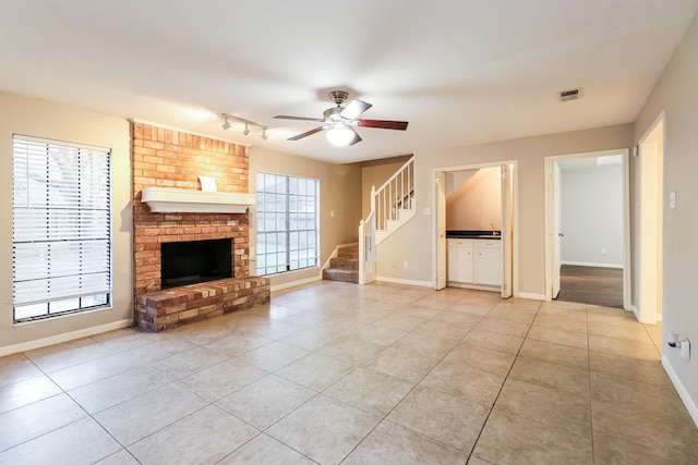 unfurnished living room with a fireplace, light tile patterned floors, track lighting, and ceiling fan