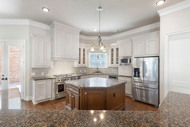 kitchen with high end appliances, a center island, hanging light fixtures, white cabinets, and ornamental molding