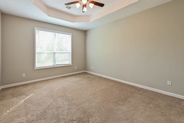 carpeted spare room with a raised ceiling and ceiling fan