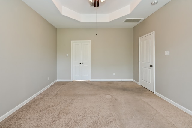 empty room featuring carpet, ceiling fan, and a raised ceiling