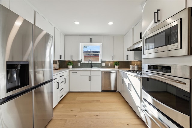 kitchen with decorative backsplash, light wood-type flooring, stainless steel appliances, exhaust hood, and white cabinets