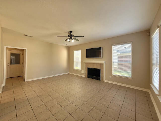 unfurnished living room featuring a tiled fireplace, ceiling fan, light tile patterned floors, and a healthy amount of sunlight