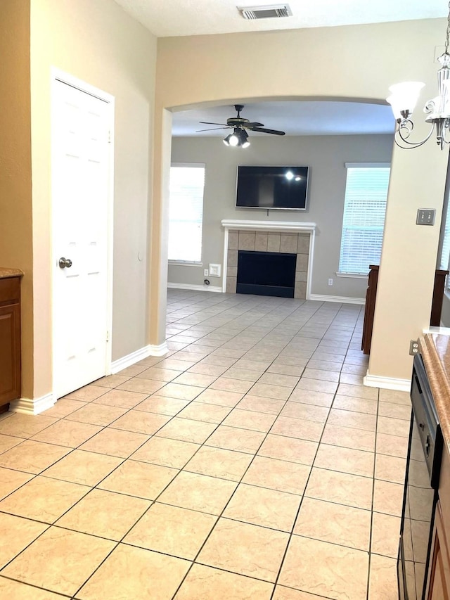 unfurnished living room featuring a tiled fireplace, light tile patterned flooring, and ceiling fan with notable chandelier