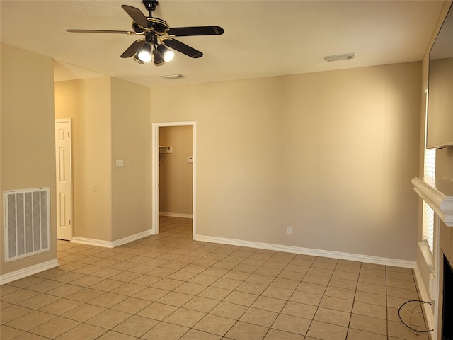 tiled empty room featuring ceiling fan and a tiled fireplace