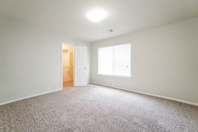 unfurnished bedroom featuring carpet flooring, connected bathroom, a spacious closet, a textured ceiling, and a closet