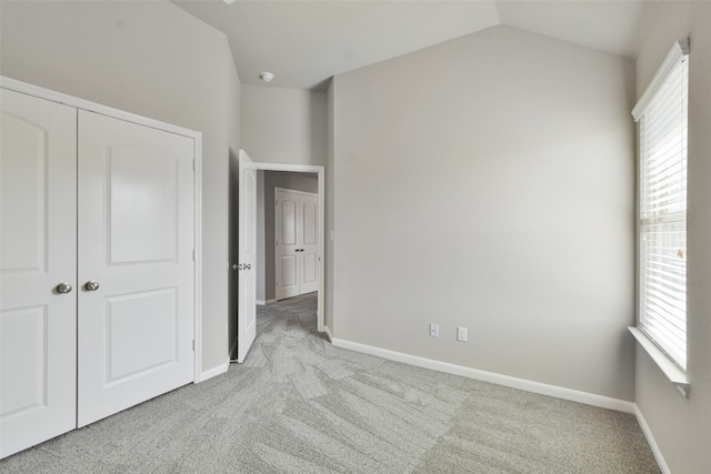 unfurnished bedroom featuring multiple windows, a closet, light colored carpet, and vaulted ceiling