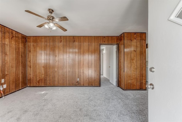 spare room featuring wooden walls, ceiling fan, and light colored carpet