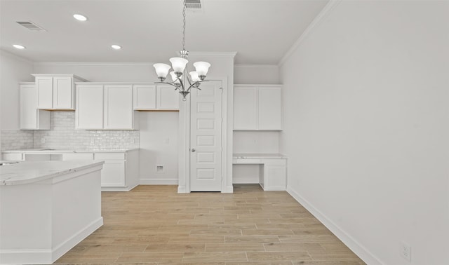 kitchen with ornamental molding, built in desk, light stone countertops, and white cabinets