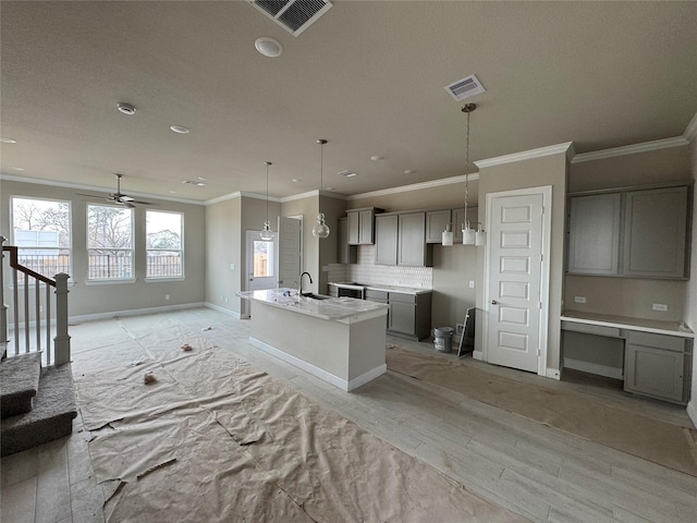 kitchen featuring sink, gray cabinets, hanging light fixtures, an island with sink, and decorative backsplash