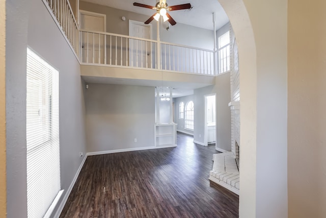 unfurnished living room featuring a fireplace, ceiling fan, dark hardwood / wood-style flooring, and a high ceiling